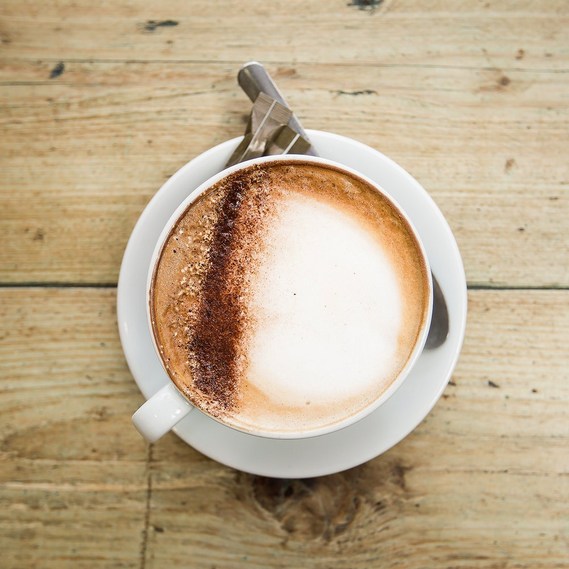 Overhead shot of a cappuccino on a wooden table with a teaspoon and brown sugar on the saucer 