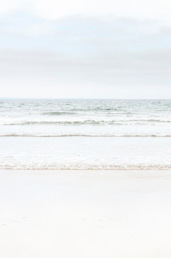 Portrait photographic image. Pale blue seascape, looking into waves from a sandy beach. 