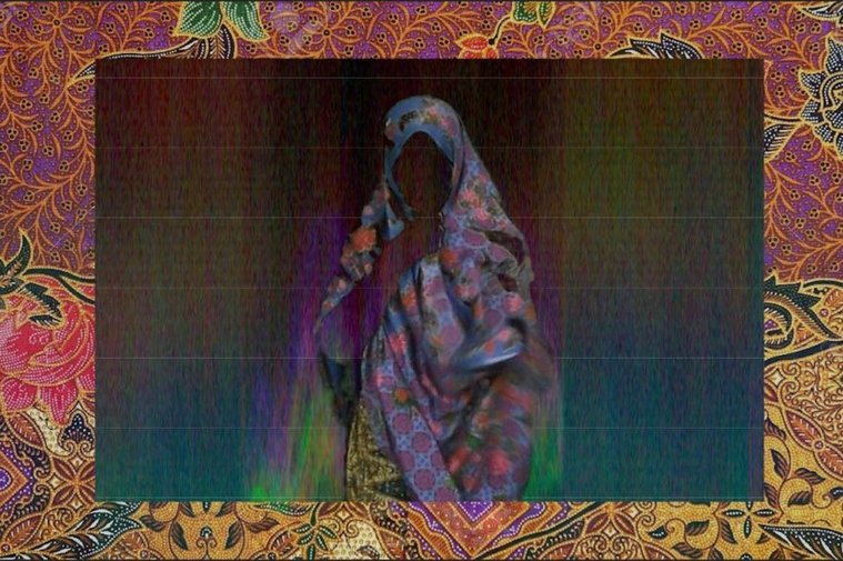 figure with cloth covering body and head, within an indistinct dark colored rectangle, face is in shadow. This is centered over a patterned, red and pink flowered cloth frame.