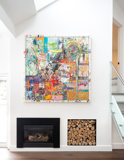 Detail of a feature wall in a bright, modern, Sandi-design inspired chalet showcasing a large, colourful abstract painting over a built-in fireplace and wood storage nook. Photographed by Interior Photographer Heather Goldsworthy