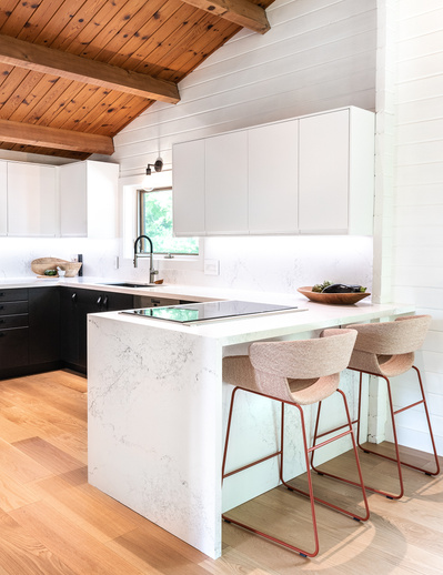 Warm, modern kitchen in a renovated chalet with marble countertops and bard seating area, custom cabinetry and rich, wood ceilings– photographed by Interior Photographer Heather Goldsworthy