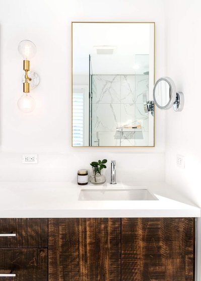 Detail of a bright, modern bathroom vanity with custom, dark wood cabinetry, marble tile and counter and gold light fixtures and accents- photographed by Interior Photographer Heather Goldsworthy