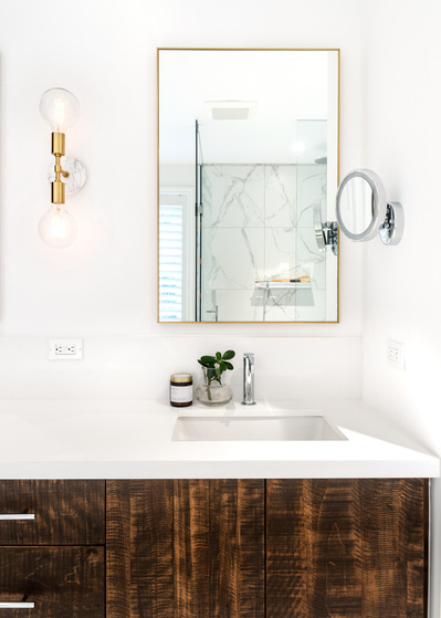 Detail of a bright, modern bathroom vanity with custom, dark wood cabinetry, marble tile and counter and gold light fixtures and accents- photographed by Interior Photographer Heather Goldsworthy