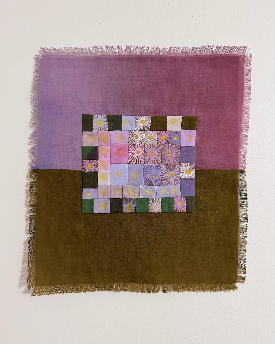 A small wall hanging with frayed edges. The  central motif is a patchwork of small squares that each depict a hand painted daisy. The background is dived in half with a purple gradient on top and olive green fabric on bottom. 