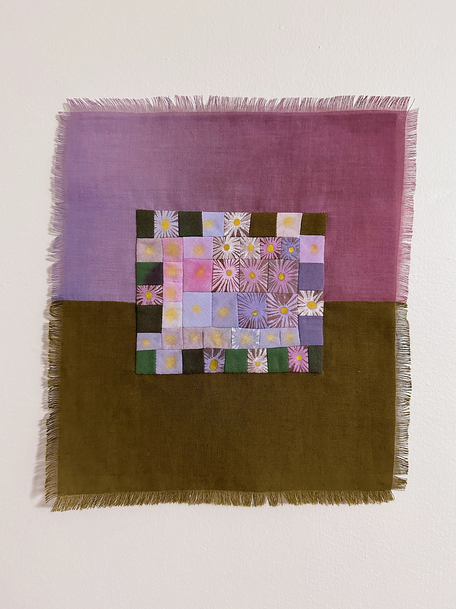 A small wall hanging with frayed edges. The  central motif is a patchwork of small squares that each depict a hand painted daisy. The background is dived in half with a purple gradient on top and olive green fabric on bottom.