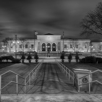Nighttime view of Detroit Institute of Arts building. Streaking clouds in long exposure create a dynamic effect. Black and white composition highlights architectural details. Handrails from Detroit Public Library guide the eyes with elegant leading lines