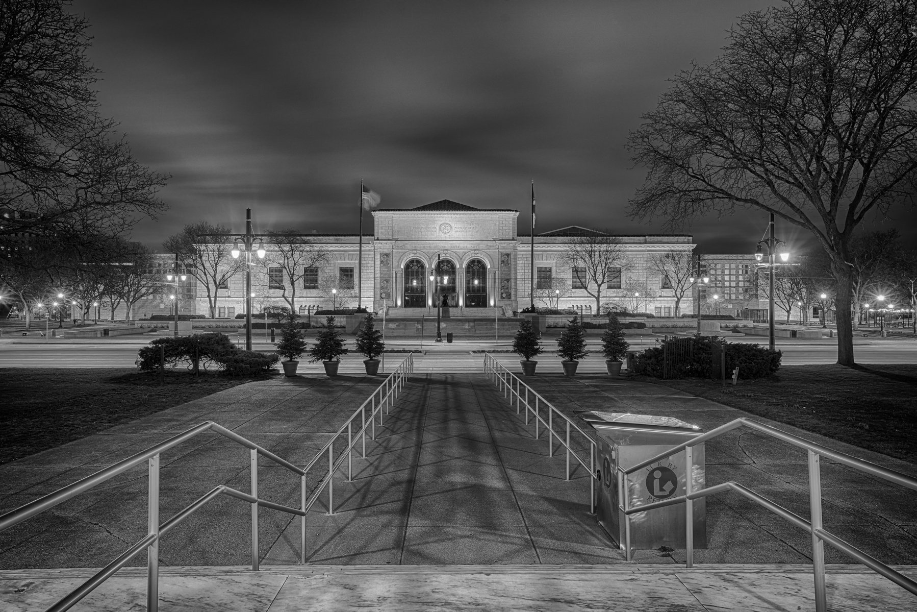 Nighttime view of Detroit Institute of Arts building. Streaking clouds in long exposure create a dynamic effect. Black and white composition highlights architectural details. Handrails from Detroit Public Library guide the eyes with elegant leading lines