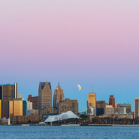 Sunrise over Belle Isle, Detroit, Michigan, with a band of pink color illuminating the top half of the frame. A captivating lunar eclipse is visible slightly above the city