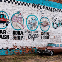 Vintage car parked in front of a large mural in Detroit, featuring the words 'Enjoy Detroit.' The mural adds vibrant colors and character to the scene, while the classic Buick car adds a touch of nostalgia and charm