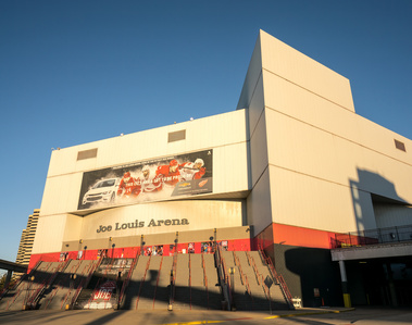 Captivating Detroit sunrise illuminating the former home of the Detroit Red Wings, Joe Louis Arena, now demolished. The shadow of the Detroit People Mover stretches across the frame, adding intrigue. The prominent steps, once climbed to enter the game, ev