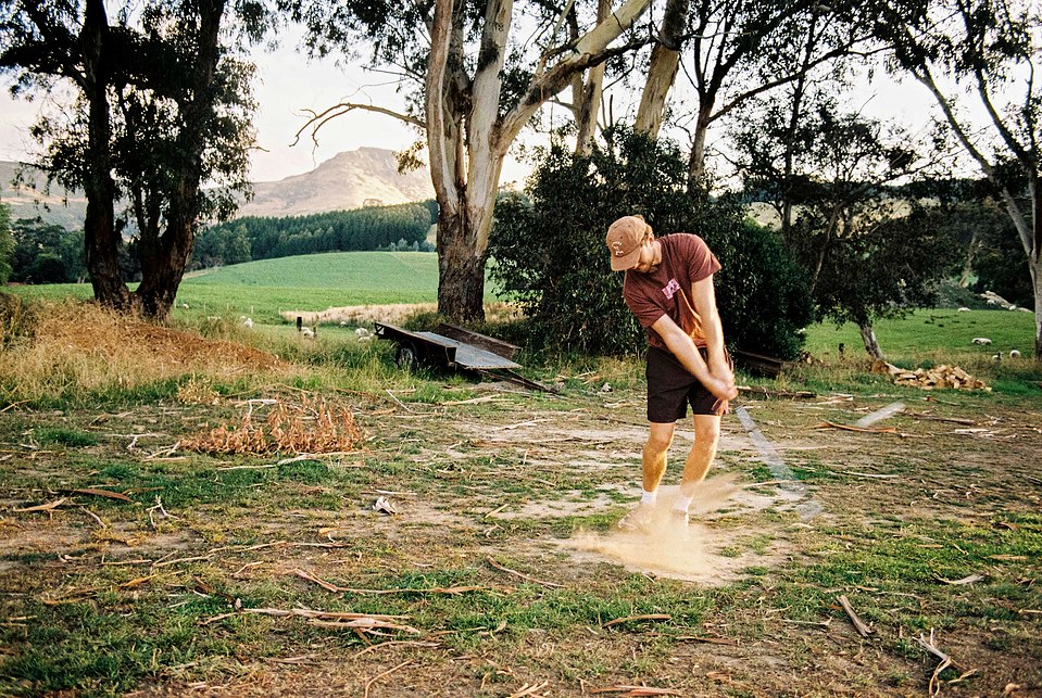 A front-angle action shot of a golfer striking the ball, with a sweeping landscape behind him. Shot on 35mm film using the Canon AE-1 Program and Tokina 28mm f/2.8 FD lens.