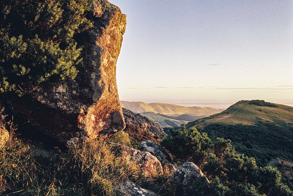 A large boulder in the foreground with the Pacific Ocean and Christchurch visible in the distance. The Canon AE-1 Program captures the wide-angle landscape on 35mm film.