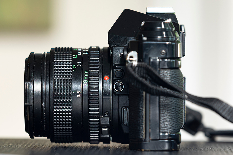 A side profile of the Canon AE-1 Program, highlighting its compact body and Tokina 28mm f/2.8 FD lens. The textured grip and manual focus ring enhance handling.