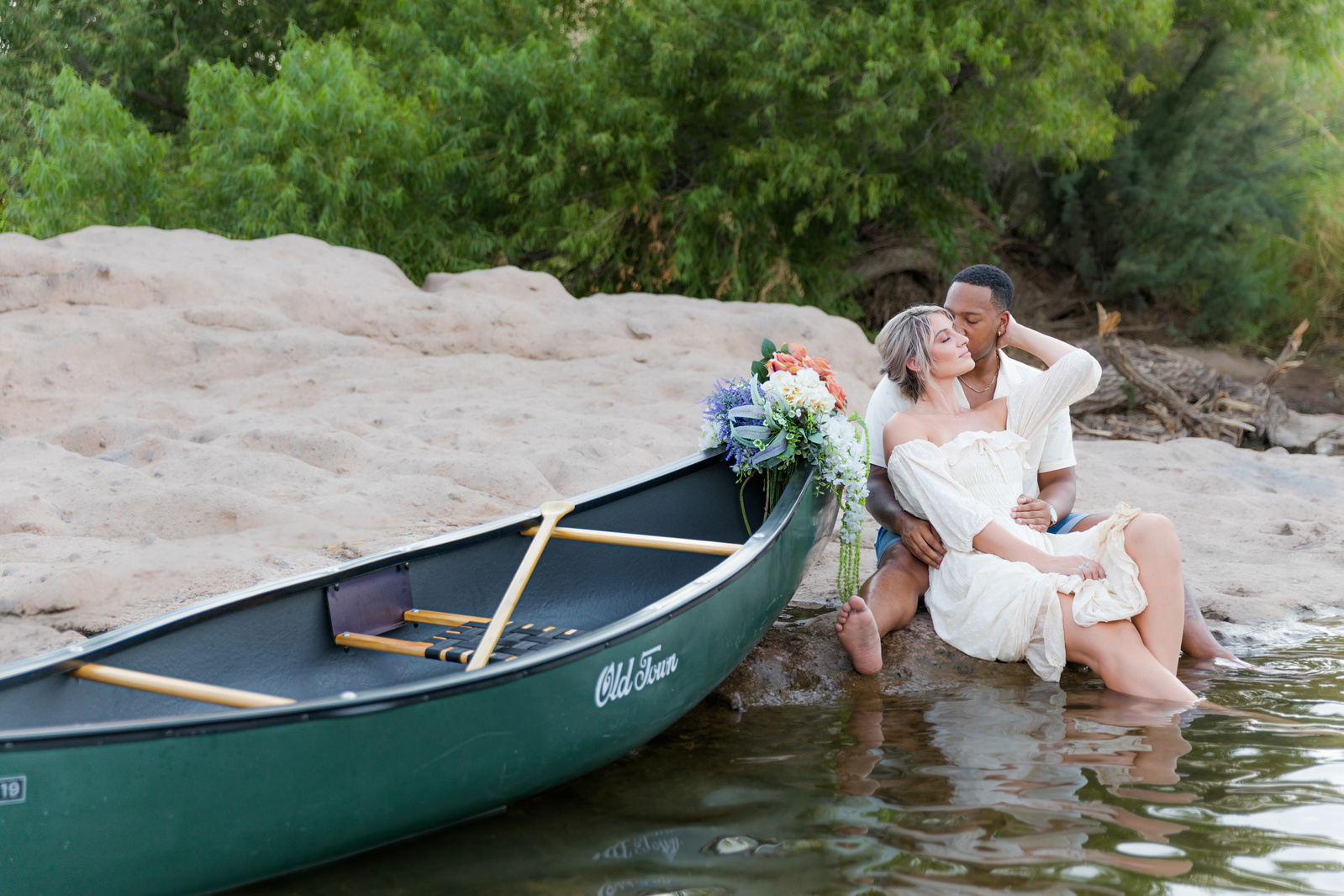 A couple sitting next to a lake by a canoe