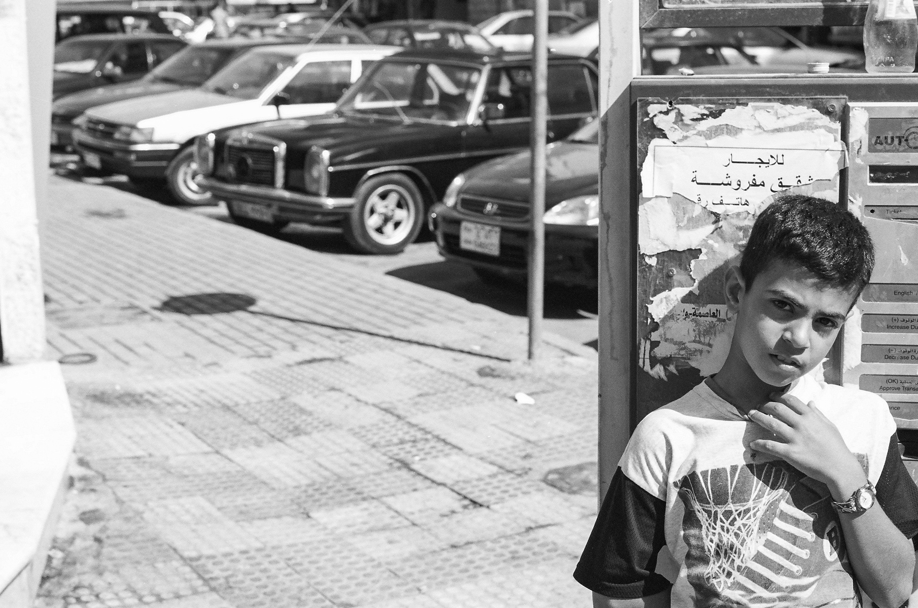 Black and white portrait of a boy standing in front of a street sign in Amman, Jordan.