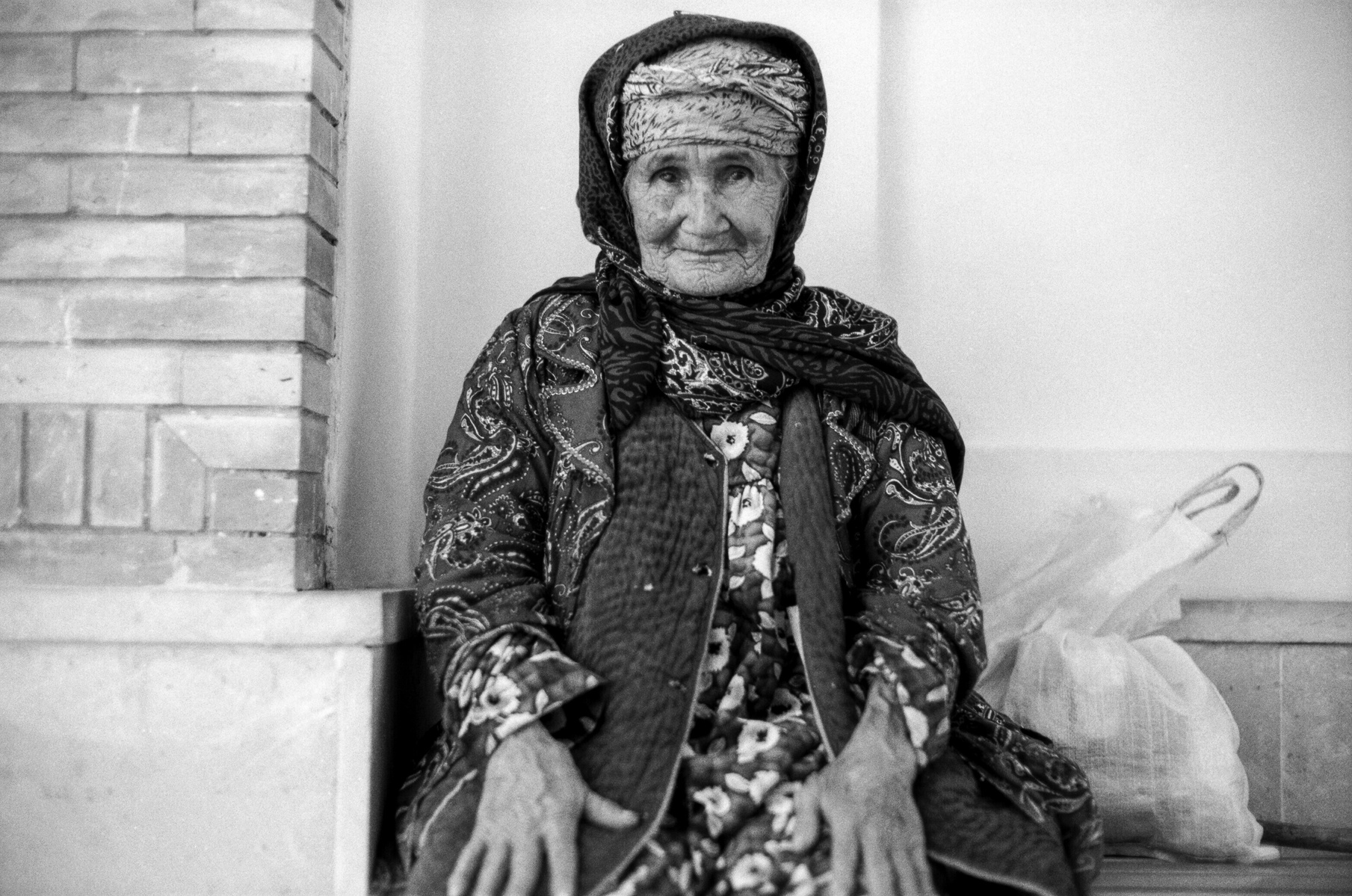 A black and white image of an old Uzbek woman sitting in a courtyard in Samarkand, Uzbekistan.