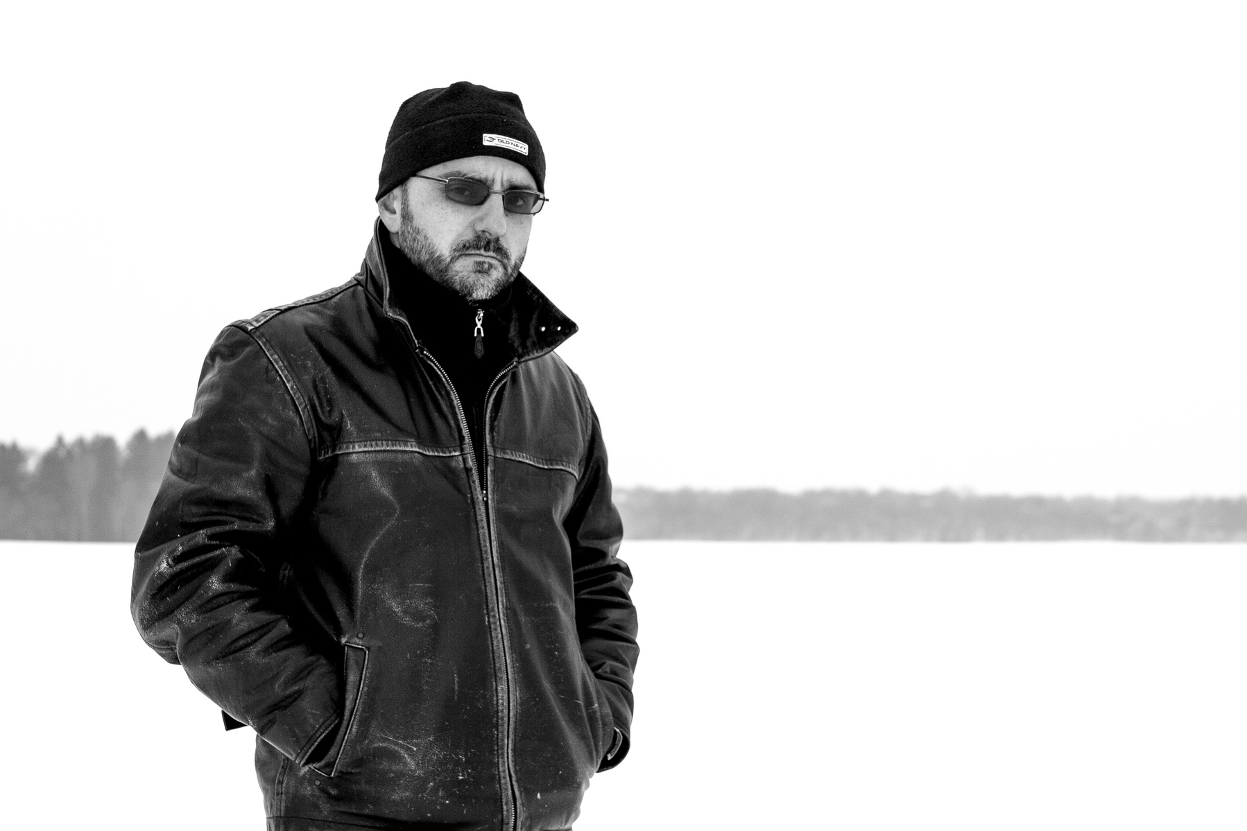 Black and white image of a man in leather jacket in front of a wintery landscape