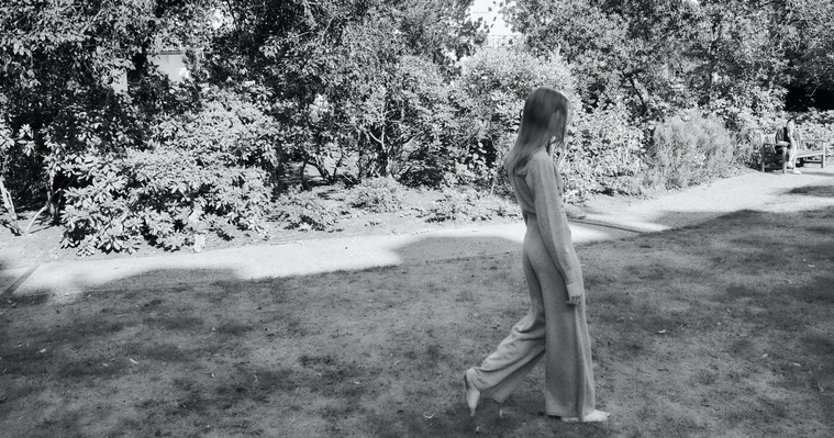 Black and white photo of a girl walking in a garden in relaxing apparel.