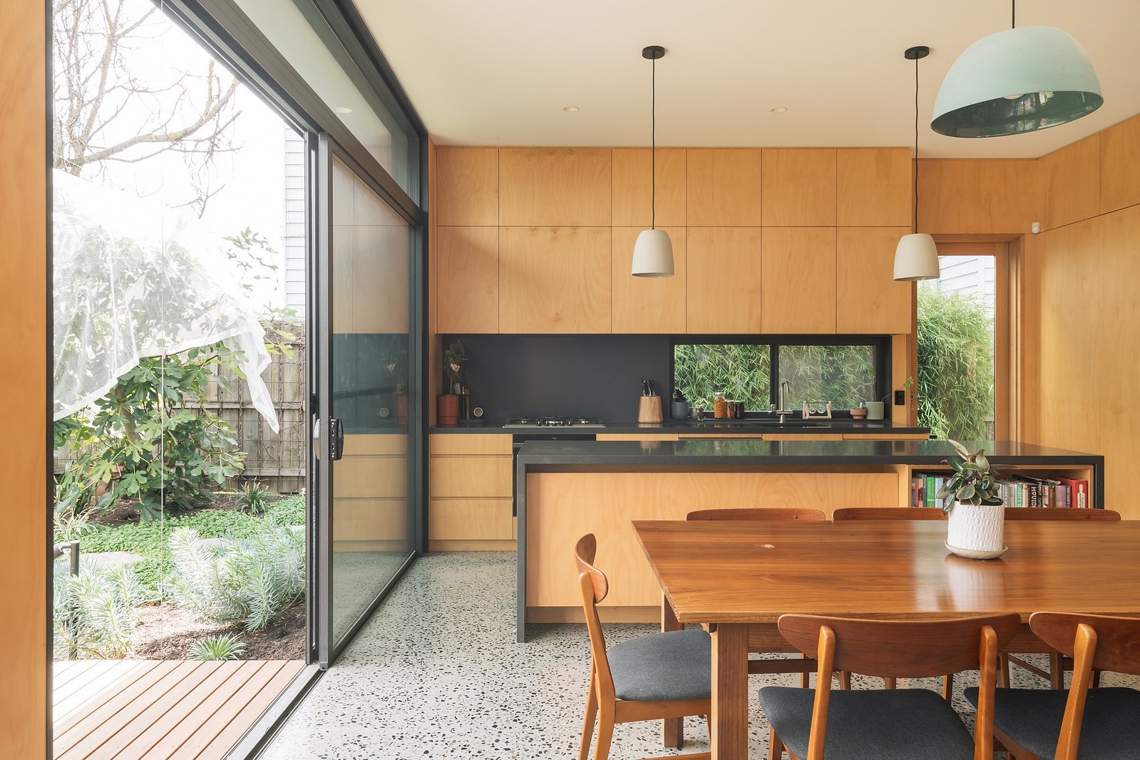 Large sliding doors open kitchen dining space out to deck and garden beyond