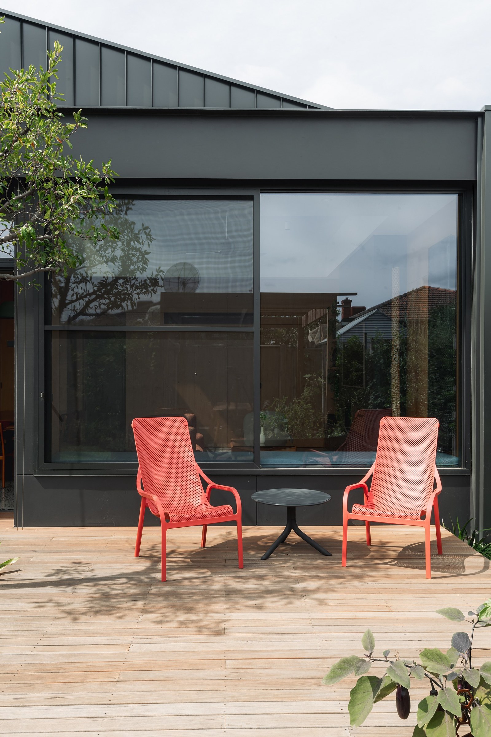 Two red seats on a deck in front of a new external building facade of black metal