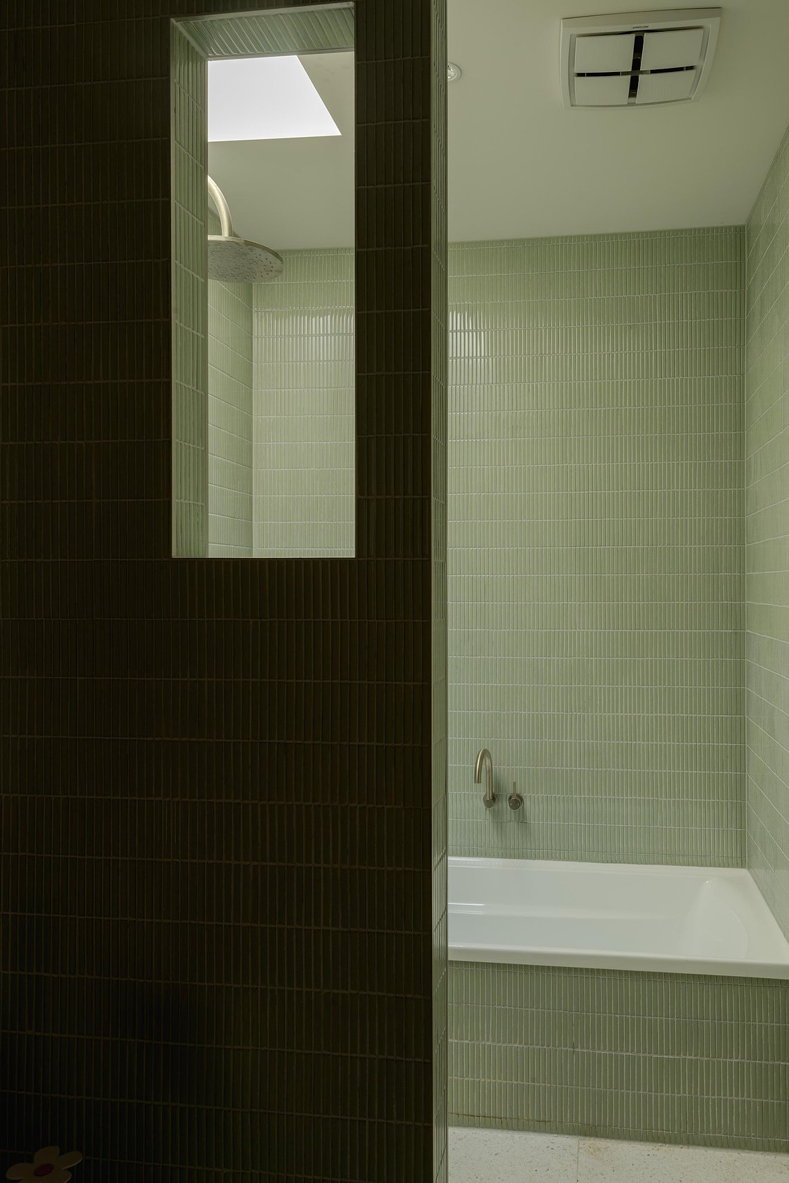 Shower area with fine tiles and opening with shower head seen. A skylight above provides natural light into the space. Sustainable living in Brunswick