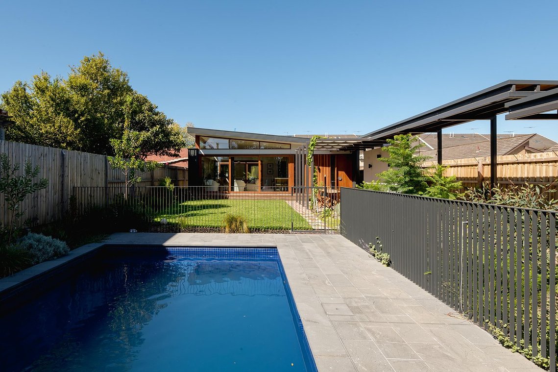 Large pool in a garden with a covered walkway to the right and a new house beyond the garden space. Sustainable living in Brunswick