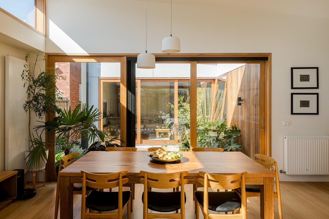Large courtyard beyond where a family dinner table is located, with greenery growing in the house and in the courtyard. Sustainable living in Brunswick