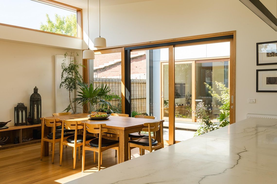 Family dining area looks out onto a central courtyard with plants growing in the distance. Sustainable living in Brunswick