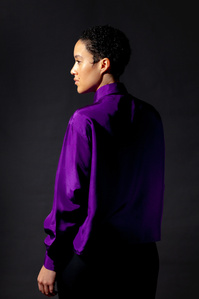 Female model wearing a purple silk shirt by Marlena Frank. Back turned towards camera looking to the left of the frame
