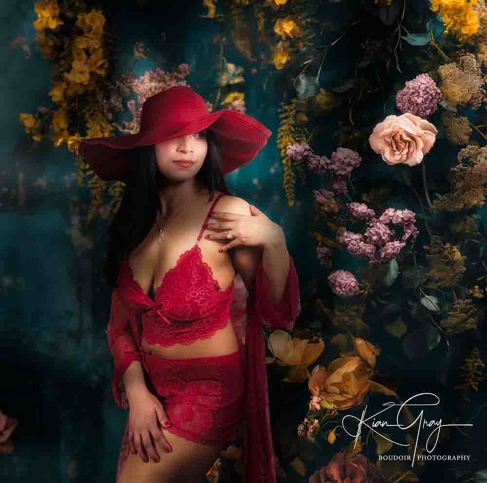 Romantic boudoir image set against an enchanted floral background, highlighting red lace lingerie and dreamy lighting.