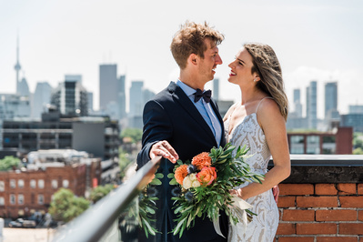 A bride and groom facing each other on a rooftop patio in front of the Toronto city skyline.