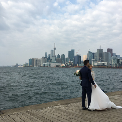 A bride and groom standing by the water with the Toronto skyline in the distance.