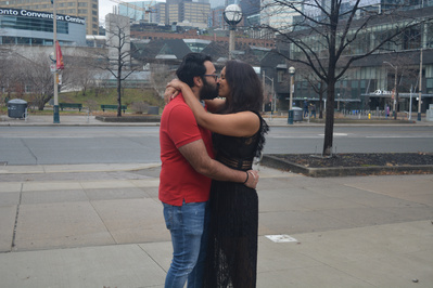 A newlywed couple wearing casual clothing kissing on a city street.