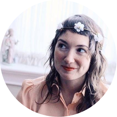 An image of Molly smiling softly at someone  out of frame and wearing a peach shirt and flower crown.