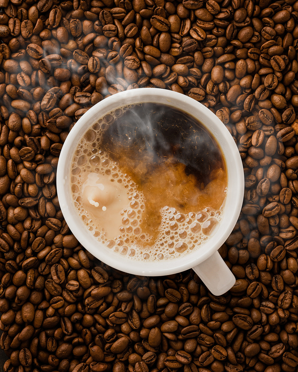 Image of hot steaming coffee being splashed with milk or cream on a bed of freshly roasted coffee beans photographed by Texas-based commercial photographer Jason Barnes
