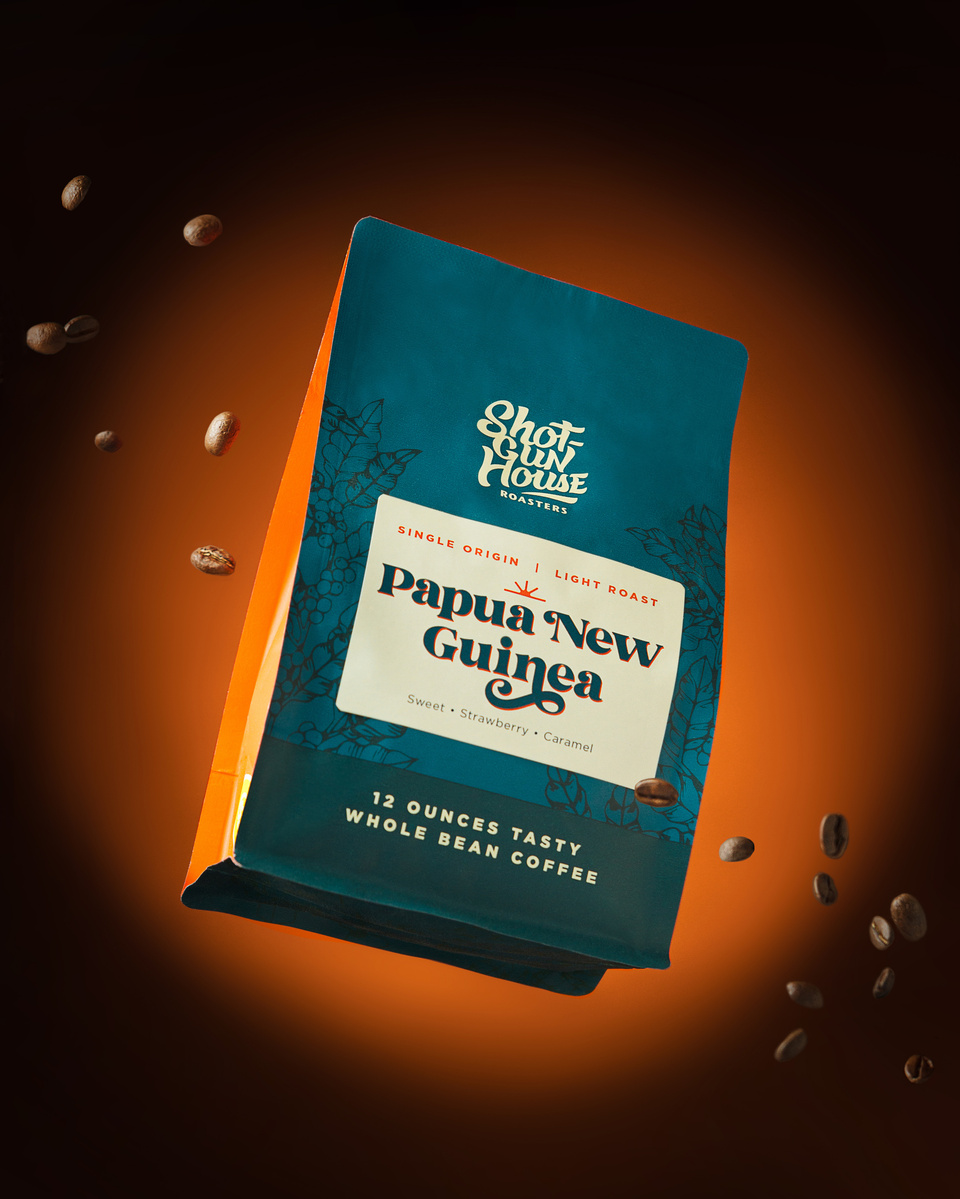 Image of Shotgun House Roasters bag of coffee on orange background suspended in air with flying coffee beans around it photographed in San Antonio, TX by commercial advertising photographer Jason Barnes