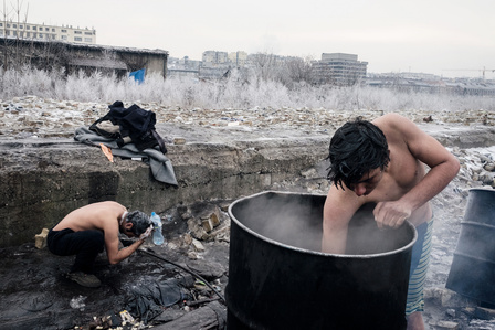 Two Afghan boys improvise a shower outside the abandoned warehouses of Belgrade station, where approximately 1200 people live crammed together in freezing temperatures, lacking water, electricity, and sanitary facilities.