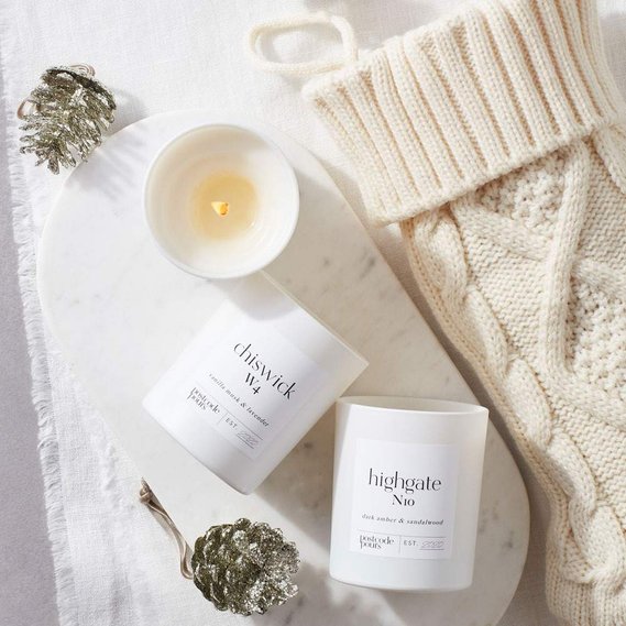 Christmas candle photography, three candles with a beige knitted Christmas stocking and silver decorations on a white linen background