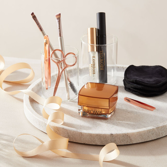 Minimal Christmas beauty product photography with gold ribbon around the London Brow products set on a marble tray.