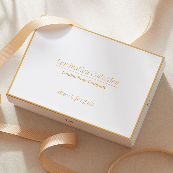 Luxury gifting image with gold ribbon around a white box in dappled sunlight