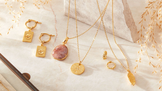 Jewellery photography, gold necklaces and earrings on a neutral colour stone background  with shadows and reflections.