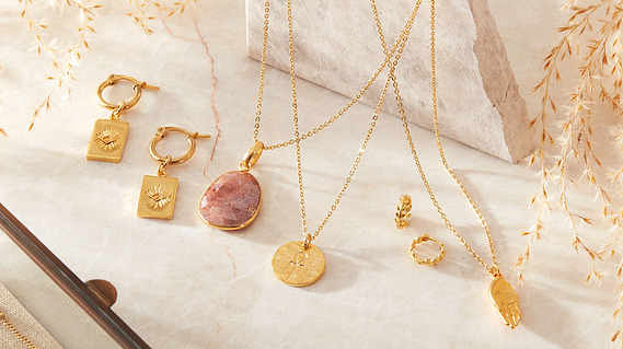 Jewellery photography, gold necklaces and earrings on a neutral colour stone background  with shadows and reflections.