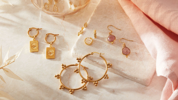 Jewellery photography, gold earrings on a neutral colour stone background with shadows and reflections