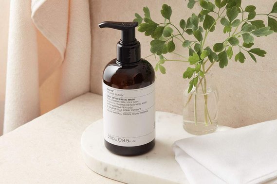 beauty product photography of a pump facial wash bottle on a bathroom shelf with fresh foliage in a vase