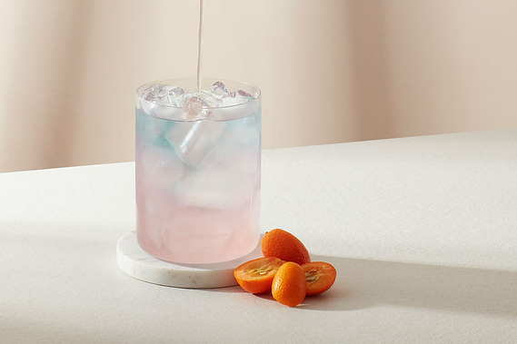 A cup of Jasmine Sapphire Needle Iced tea being poured.  Tabletop scene on a neutral tabletop with daylight shadows