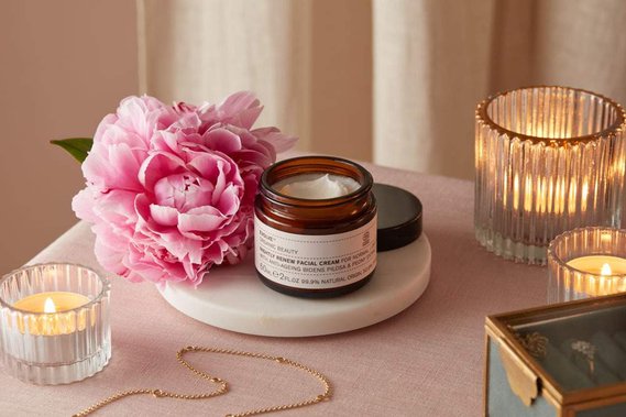 Christmas product photography of a moisturiser lit by candle-light on a pink linen  background