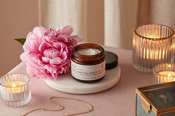 Christmas product photography of a moisturiser lit by candle-light on a pink linen  background