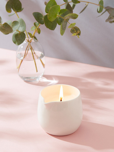 Lifestyle product photography of a massage candle on a pink background in dappled shadow