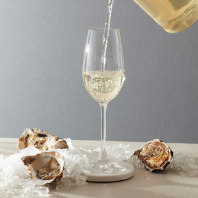 A flute glass of cold brew tea with oysters and crushed ice on a tabletop with a grey background