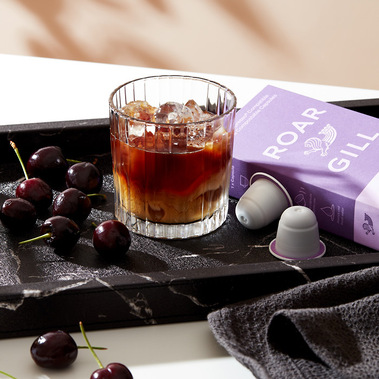 Coffee produc photography of an iced coffee served on a black tray with fresh cherries.
